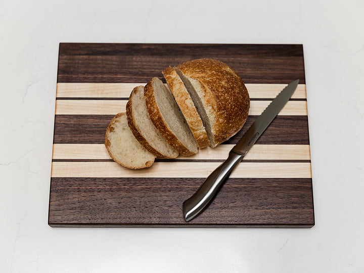 Sliced loaf of bread on a walnut and maple edge grain cutting board with a knife