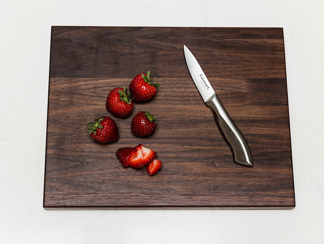 walnut edge grain cutting board with strawberries and a knife on a white background