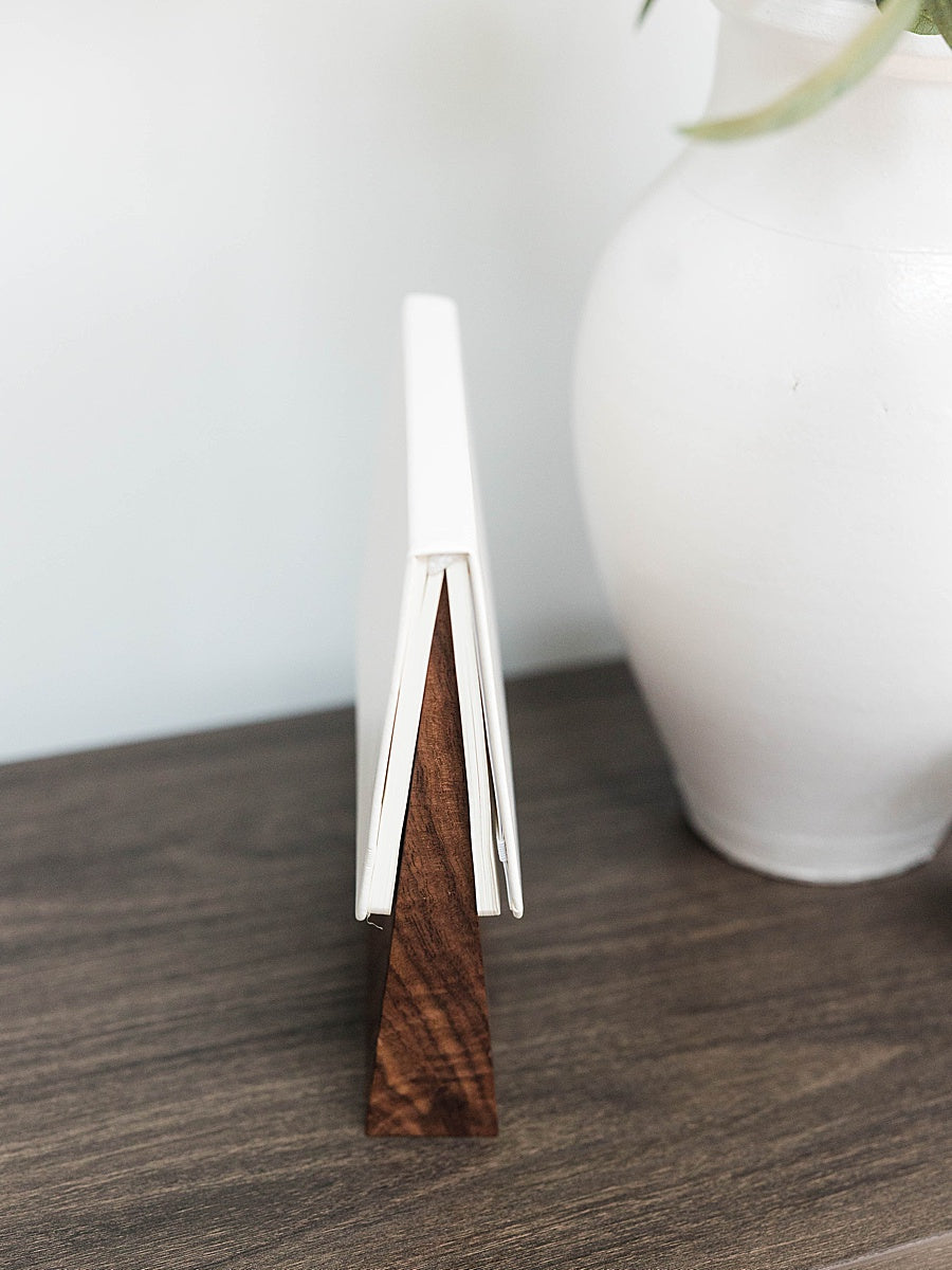 Solid walnut book wedge with white journal on top sitting wood table with a white vase in the background