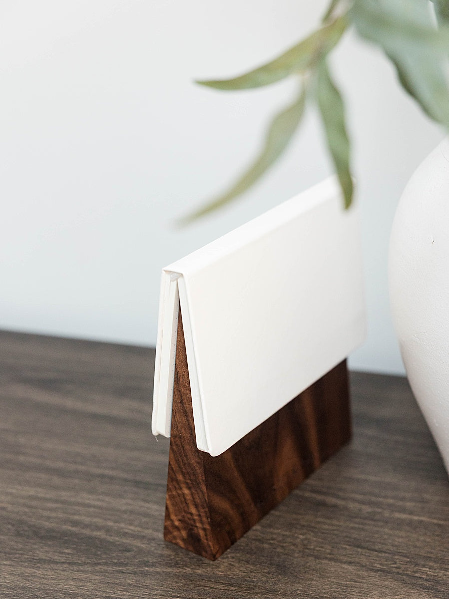 Solid walnut book wedge with white journal on top sitting wood table with a white vase in the background