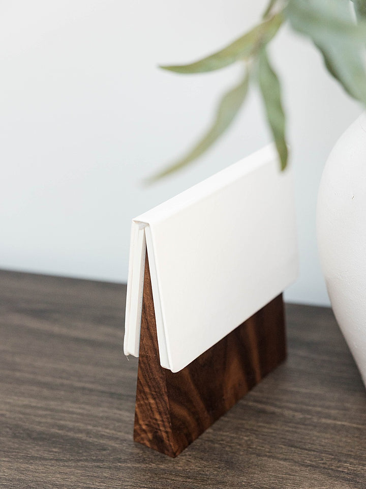 Solid walnut book wedge with white journal on top sitting wood table with a white vase in the background