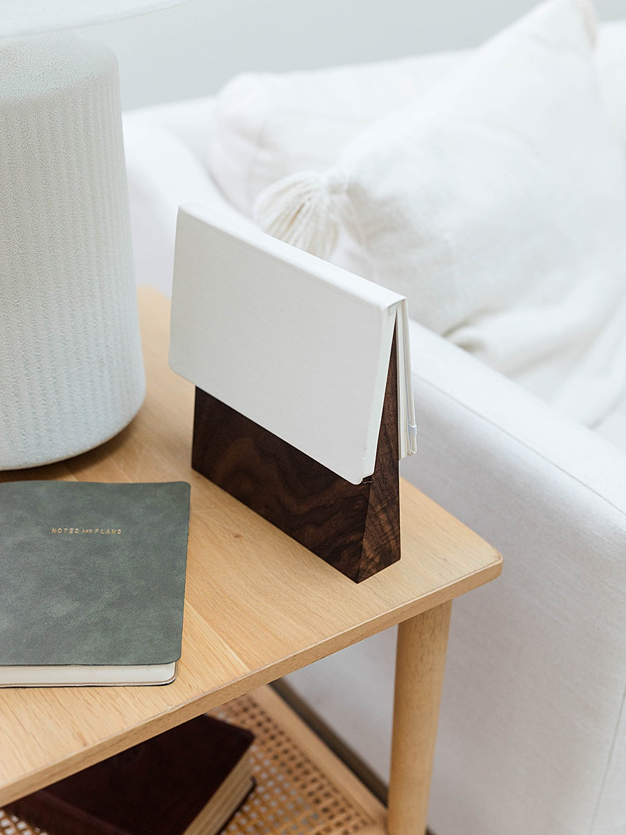 Solid walnut book wedge with white journal on top sitting on a side table