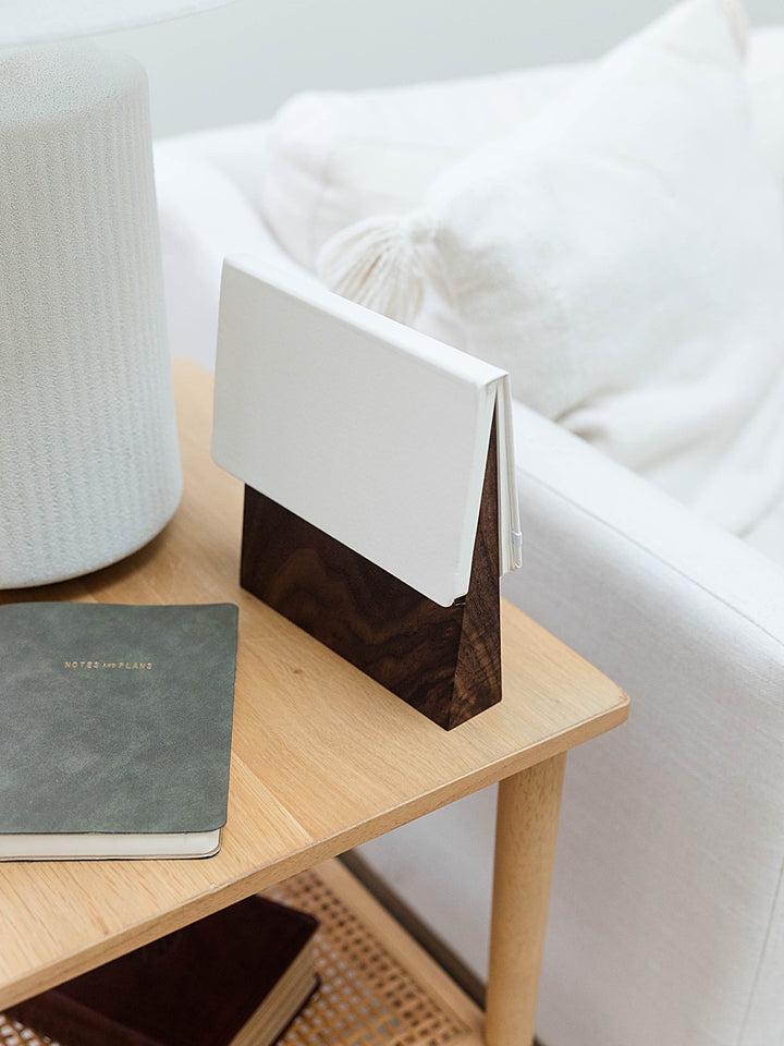 Solid walnut book wedge with white journal on top sitting on a side table