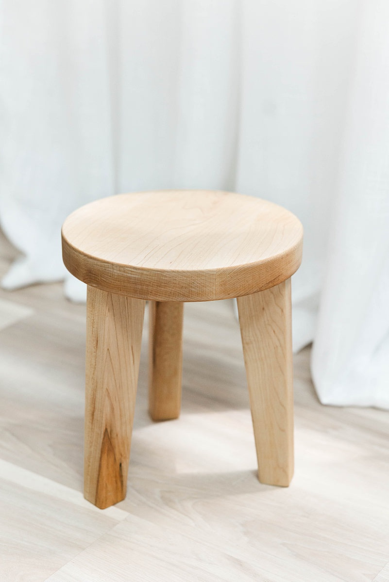 Solid maple  stool on a light-colored surface with a white curtain background