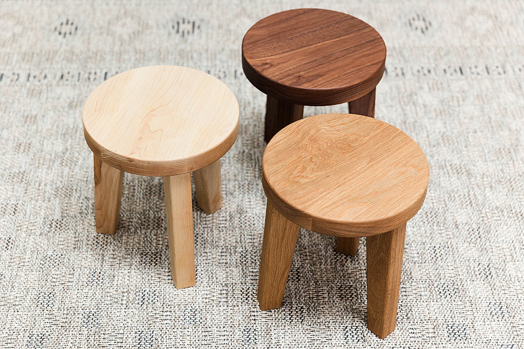 Three solid wooden stools of maple, walnut and white oak on a textured surface