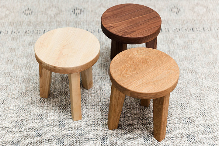 Three solid wooden stools of maple, walnut and white oak on a textured surface