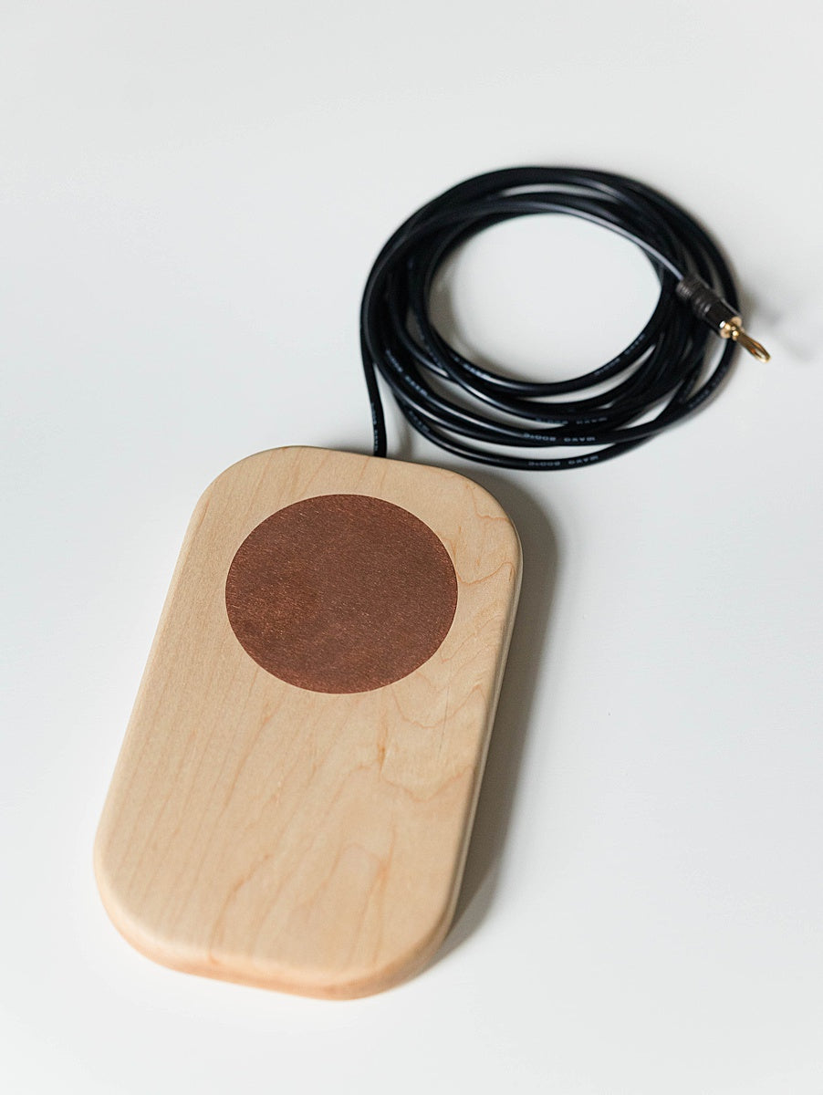 Maple grounding board with a circular copper component and black cable on a white background