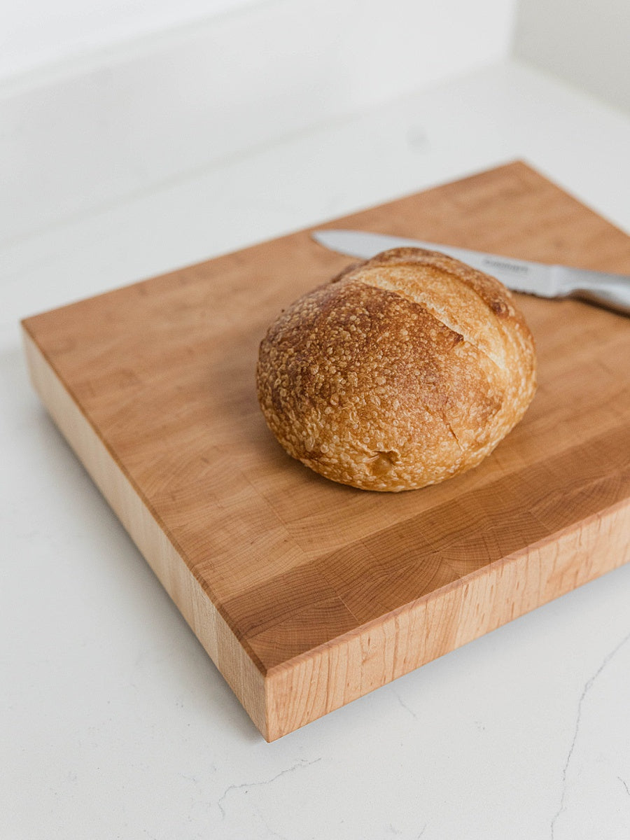 Loaf of bread on a wooden cutting board with a knife on a light background