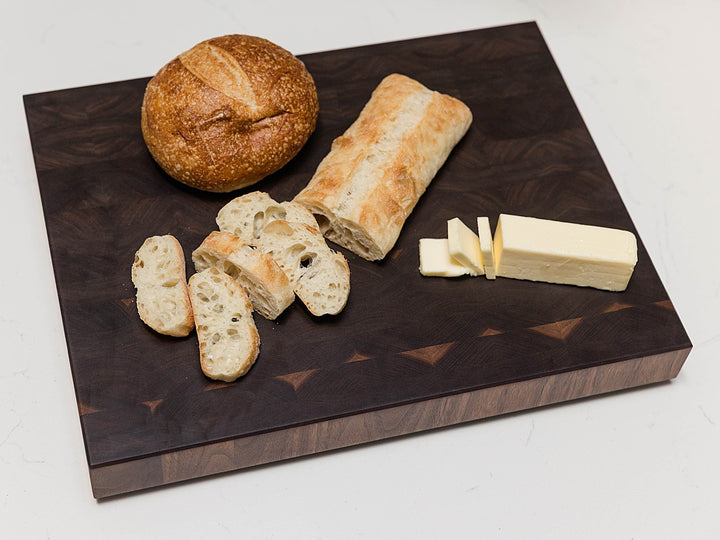 Walnut end grain cutting board with bread and butter on a white background